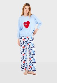 Sudadera azul claro con un diseño de corazón rojo y detalles en blanco, combinada con pantalones anchos estampados en azul, rojo y negro.