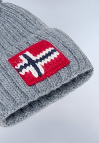 Harmaa neulepipo, jossa on taitettu reunus ja punainen merkki, jossa on valkoinen ja sininen pohjoismainen risti -kuvio. Tekstuuri on paksu ja mukava.