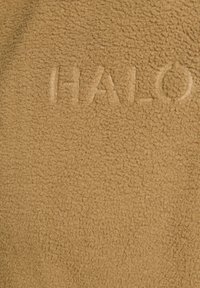 Bruine fleece stof met een zachte, gestructureerde uitstraling met het reliëfwoord "HALO." Glad, warm en uniform van kleur.