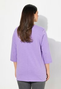 Lila lätt topp tillverkad av mjukt tyg, med trekvartslånga ärmar, rundad halsringning och en vertikal söm på baksidan.