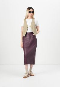 En tett beige vest over en hvit skjorte, sammen med en mørk lilla skinnskjørt. Beige joggesko med kremfargede sokker fullfører antrekket.