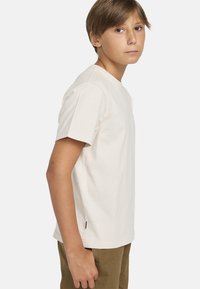 Kauranvärinen puuvillainen t-paita, jossa on pyöreä kaula-aukko ja lyhyet hihat. Paidassa on suora leikkaus ja pieni logo-tagi sivusaumassa.