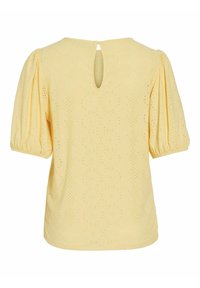 Blouse jaune avec des manches courtes bouffantes, un col rond et un détail en fente à l'arrière. Présente des motifs découpés au laser sur l'ensemble.
