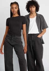 Svart tettsittende t-skjorte og mørk grå oversized skjorte, kombinert med løse mørke jeans. Stoffene ser myke ut med en glatt tekstur og minimale detaljer.