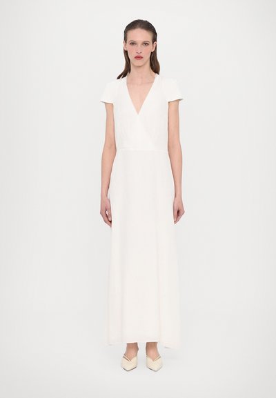 Long, white dress with a deep V-neck, short sleeves, and a fitted bodice. Smooth fabric with a subtle texture, floor-length. Square-toed beige shoes.