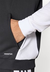 Fekete-fehér sportos kapucnis pulóver texturált anyaggal, oldalsó cipzáras zsebbel és „FORMOTION” logóval. Testhezálló mandzsetta kialakítással.