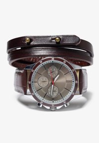 Reloj con correa de cuero marrón y esfera metálica plateada y gris, con acentos rojos, tres subesferas y un bisel metálico delgado.