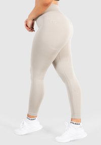 Beige hoge taille leggings met een gladde textuur, met een naadloos ontwerp en subtiele stiksels. Combineren met witte sportschoenen.