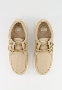 Beige Leinensneaker mit einer strukturierten Oberseite, runder Spitze und hellfarbener Sohle. Verfügt über dekorative Schnürsenkel und ein "REEF"-Logo.