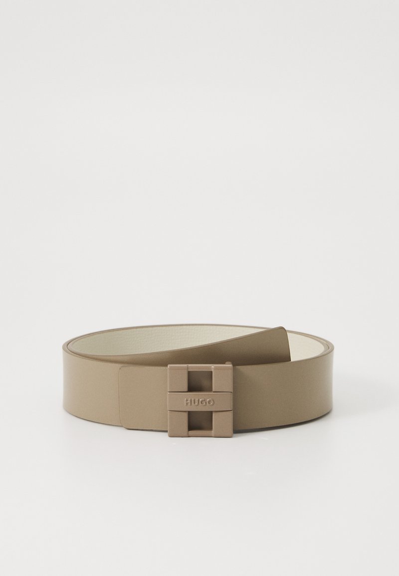 Beige szintetikus öv sima textúrával és négyzet alakú csattal, amelyen a "HUGO" felirat látható. Egyszerű és minimalista dizájn.