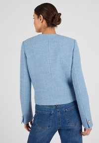 Blauwe blazer met textuur en een getailleerde silhuet, brede schouders en lange mouwen. Voorzien van een rugnaad en gouden knoopaccenten op de manchetten.