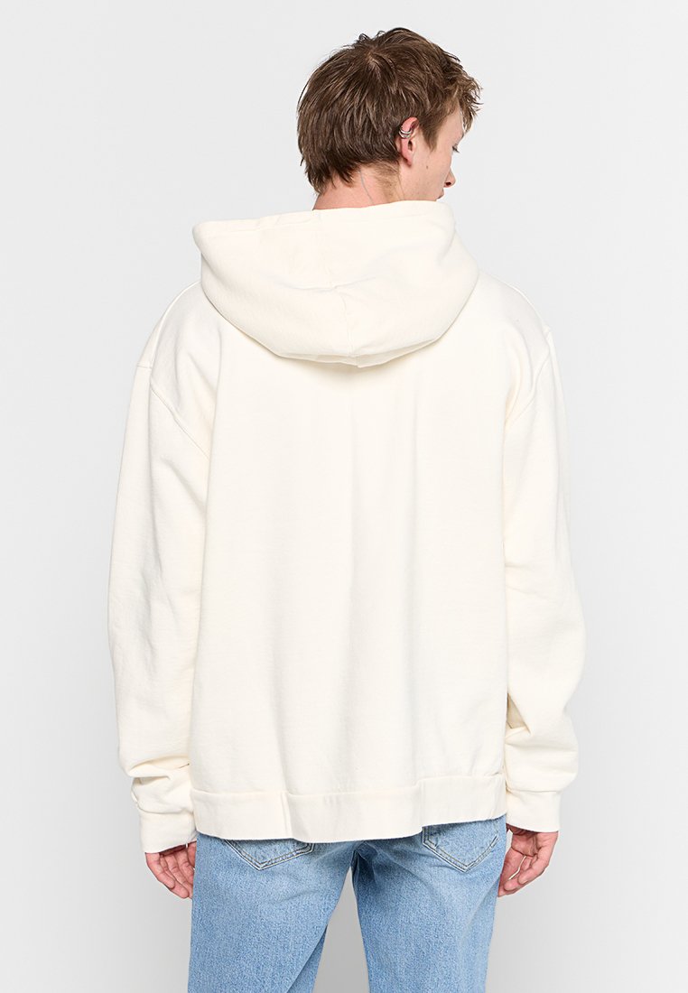 Cremefarbener Kapuzenpullover mit lockerer Passform, großer Kapuze und geripptem Saum. Hergestellt aus weichem Material, verfügt er über eingesetzte Ärmel und Nähdetails.