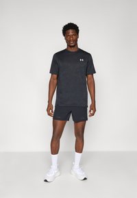 Zwarte sportieve t-shirt en shorts met een subtiel patroon. Bevat een logo op de borst, gecombineerd met witte sneakers en crew-sokken.