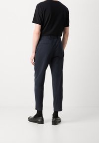 Marinblå byxor med elastisk midja, smalnande ben och framfickor. Kombinerat med svarta loafers och en svart T-shirt. Slät textur.