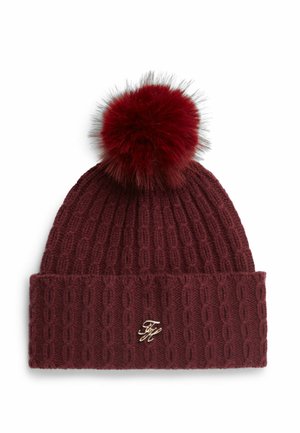 Burgunderfarvet kabelstrikket hue med en stor fluffy kvast på toppen og en lille gulddetalje med monogram på den foldede kant.
