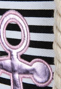 Tejido a rayas en colores negro y blanco, con un prominente emblema de ancla metálica rosa y un detalle de cuerda texturizada en el costado.