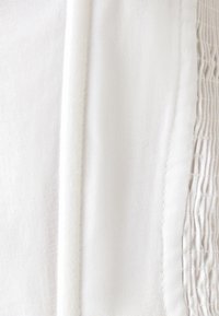 Tessuto bianco con una trama liscia, caratterizzato da una sezione arricciata a destra e un bordo dritto a sinistra, creando un contrasto visivo.