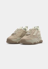 Chunky athletic sneakers with a light beige mesh upper, textured overlays, and rubber sole, featuring lace-up closure and pull tabs.