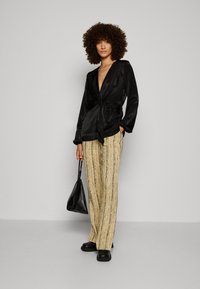 Svart satinwrap-top med långa ärmar och djup V-halsringning, tillsammans med texturerade, randiga beiga och guld vida byxor. Svart handväska som accessoar.