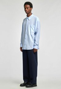 Lyseblå stripete skjorte med knapper og brystlomme, kombinert med marineblå vide bukser og svarte skinnsko.