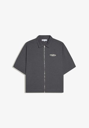 Krátka sivá košeľa z uhlíkovej farby s golierom, predným zipsom a malou nášivkou "Kings of New York" na ľavej strane hrudníka.