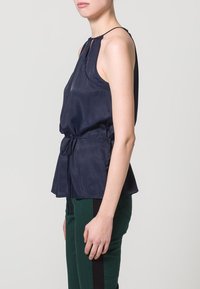 Marinblus utan ärmar i mjukt tyg, med en samlad halsringning, justerbar snörning i midjan och en avslappnad passform.