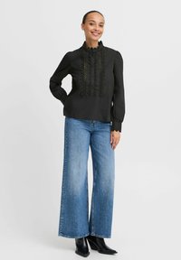 Black blouse with ruffled collar and button placket, paired with wide-leg blue denim jeans and black ankle boots.