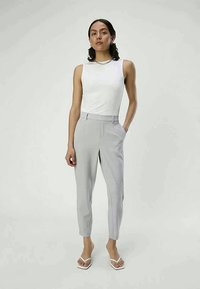Grey tailored pants with a slim fit, side pockets, and a crease down the front. Paired with a white sleeveless top and white sandals.