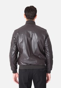 Giacca bomber in pelle marrone con colletto e polsini a coste, caratterizzata da una superficie liscia e dettagli cuciti sulla schiena.