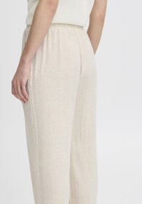 Pantalons léger beige, à taille élastique, de coupe décontractée. Le tissu est texturé avec un tissage subtil, conçu pour le confort et la liberté de mouvement.