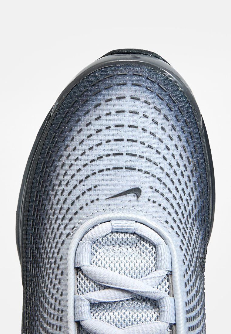 Szare i białe buty sportowe z siateczkową cholewką, teksturowanymi detalami, okrągłym noskiem i sznurowanym zapięciem. Z boku znajduje się czarne logo Nike.