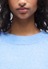 Ανοιχτό μπλε πλεκτό πουλόβερ με ριμπ ύφασμα στο λαιμό και απαλή υφή, σχεδιασμένο με μακριά μανίκια και άνετη εφαρμογή.