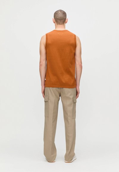 Haut en tricot sans manches orange associé à un pantalon cargo beige avec poches latérales et coupe décontractée, présenté de dos.