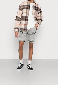 Koszula w kratkę button-up w kolorze beżowym, brązowym i pomarańczowym; biała koszulka; szare szorty dżinsowe z czterema kieszeniami; czarno-białe sneakersy.