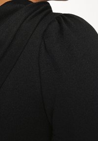 Svart tyg med en texturerad yta och samlad puffärmad detalj, som visar en närbild av ett plagg.