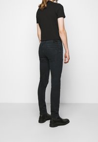 Camiseta negra de manga corta combinada con jeans ajustados azul oscuro, con una textura suave y dos bolsillos traseros. Llevada con botas negras hasta el tobillo.