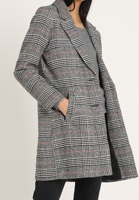 Cappotto a quadri in misto lana con motivi grigi, neri e rossi. Design doppiopetto con rever a incasso e tasche laterali.