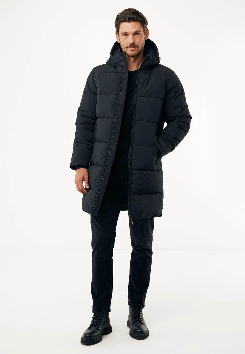 Schwarze Puffjacke mit Kapuze, mit einem gesteppte Design, Frontreißverschluss und seitlichen Taschen. Getragen über einem schwarzen Pullover und Jeans.
