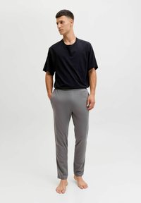 T-shirt nera a maniche corte abbinata a pantaloni slim-fit grigi chiari. Entrambi gli articoli presentano una texture liscia e un design minimalista.