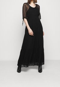 Czarna sukienka maxi z przejrzystymi bufkami na rękawach, marszczonym gorsetem i warstwową spódnicą. Wykonana z lekkiego materiału o gładkiej fakturze.