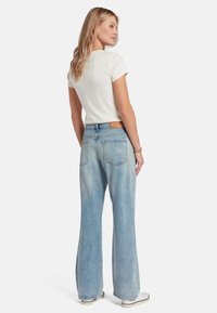 Jeans de denim de tiro alto de color azul claro con corte recto, bolsillos traseros y un parche de cuero marrón en la cinturilla. Camiseta blanca.