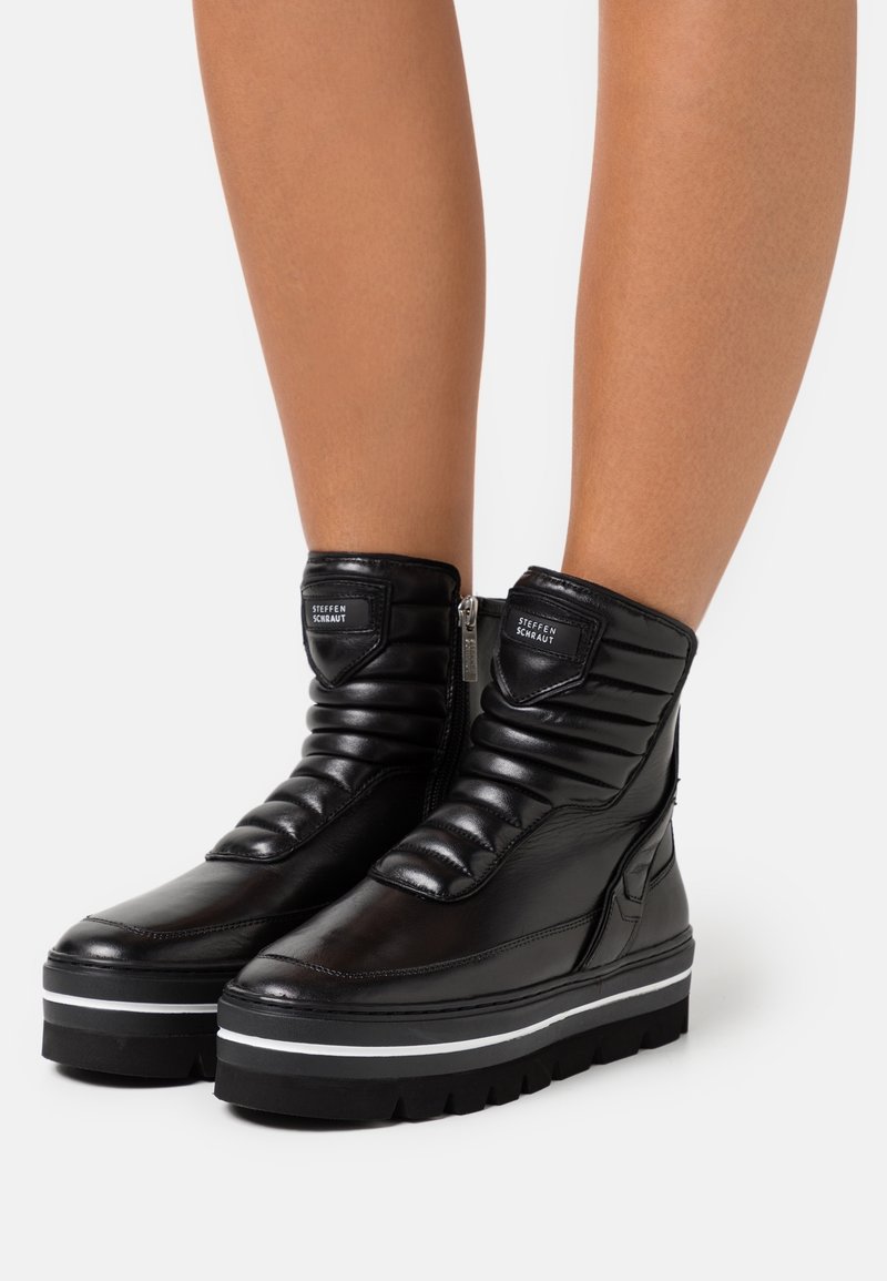 Botas de tobillo de cuero negro con detalles acolchados, cremallera lateral y suela gruesa negra con acentos en blanco.