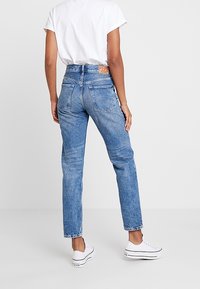 Högmidjade blå denimjeans med en urtvättad yta, rak benpassform och två bakfickor. Tillsammans med en enkel vit t-shirt och vita sneakers.