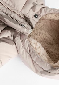 Vaalean beige-täytetty takki, jossa on lampaanvillavuori, vetoketju ja napit sekä huomaamaton abstrakti kuvio ulkomateriaalissa.