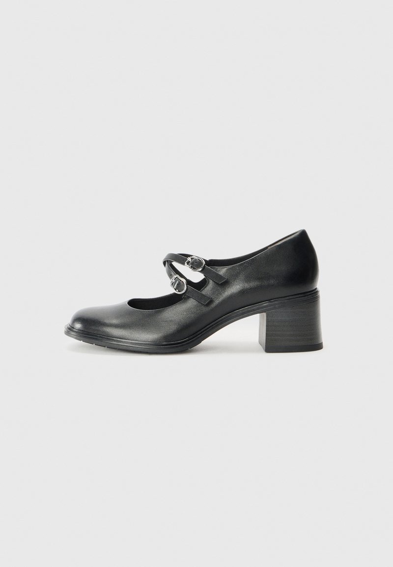 Chaussure Mary Jane en cuir noir avec double boucle et petit talon épais sur fond gris clair.