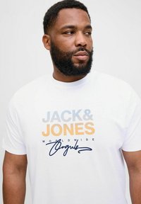 Valge puuvillane T-särk, millel on mitmevärviline tekst: "JACK & JONES" sinise ja oranži värviga, allpool on "WORLDWIDE" ja allkiri disain.