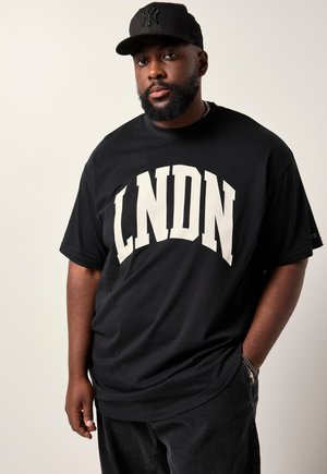 Sort t-shirt med hvid "LNDN" tekst over forsiden; parret med mørke bukser og en sort baseballkasket med logo.