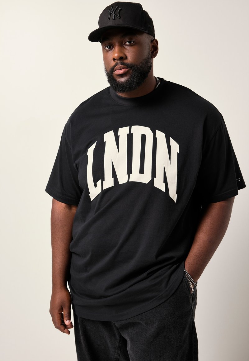 Sort t-shirt med hvid "LNDN" tekst over forsiden; parret med mørke bukser og en sort baseballkasket med logo.