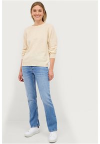 Licht beige gebreide trui met lange mouwen, ronde hals, relaxte pasvorm; gecombineerd met lichtblauwe recht gesneden jeans en witte sneakers.