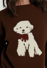 Maglione marrone lavorato a maglia con una grafica di un cane bianco che indossa una cravatta rossa, evidenziando il tessuto testurizzato e i colori a contrasto.